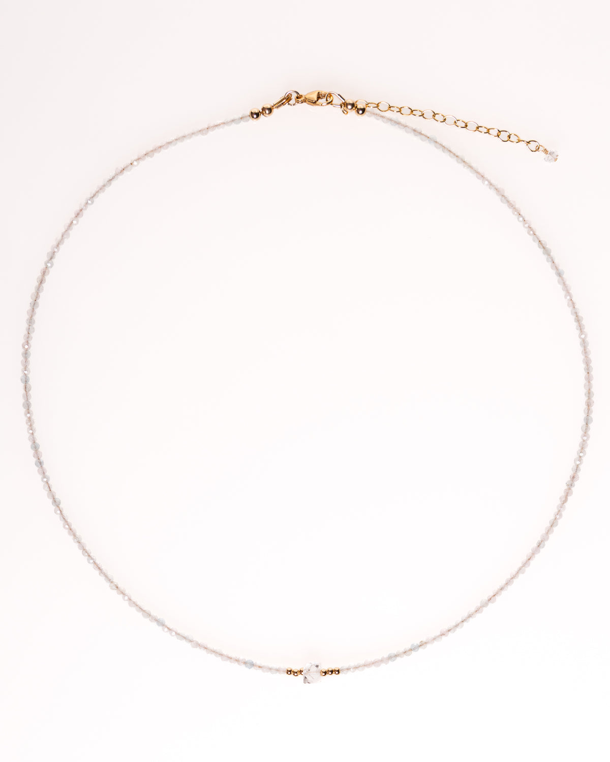 A delicate necklace with a fine silver chain, a small central clear crystal charm, and gold-toned hardware, including a clasp and extender chain, displayed on a clean white background.
