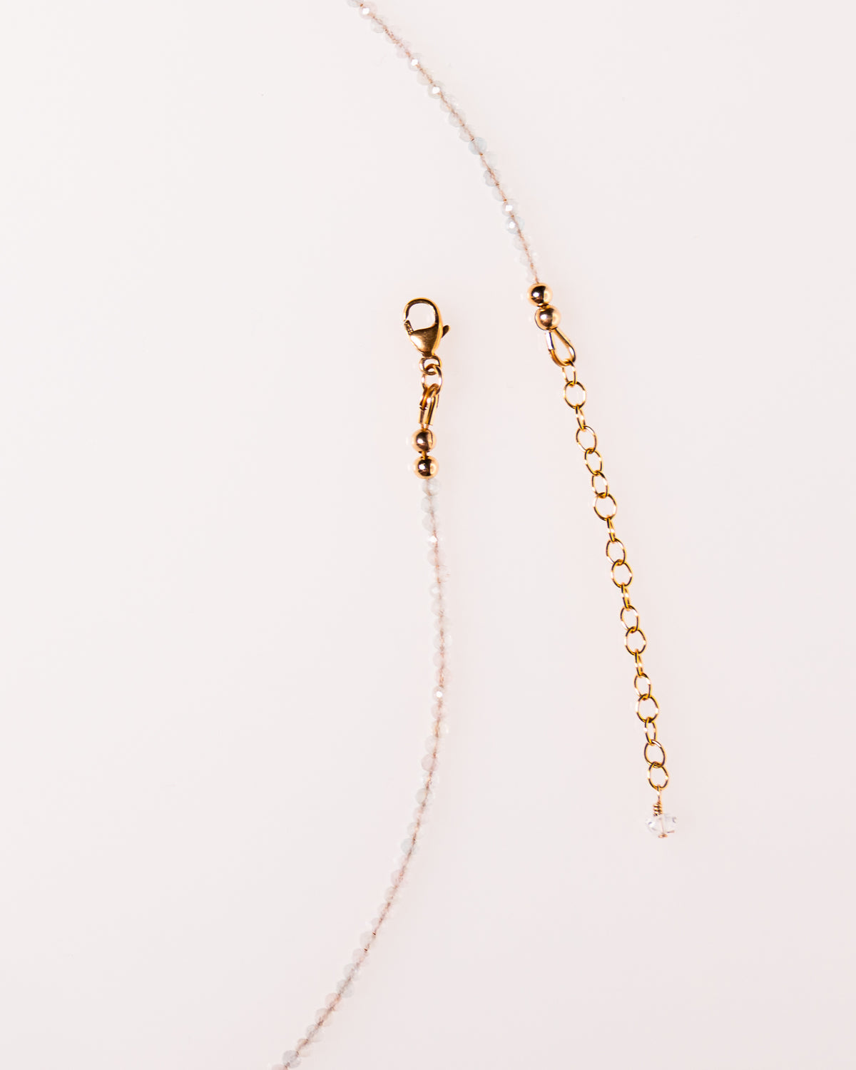 Close-up of a delicate gold-tone chain extender with a lobster clasp and a small clear crystal bead, shown on a plain white background.