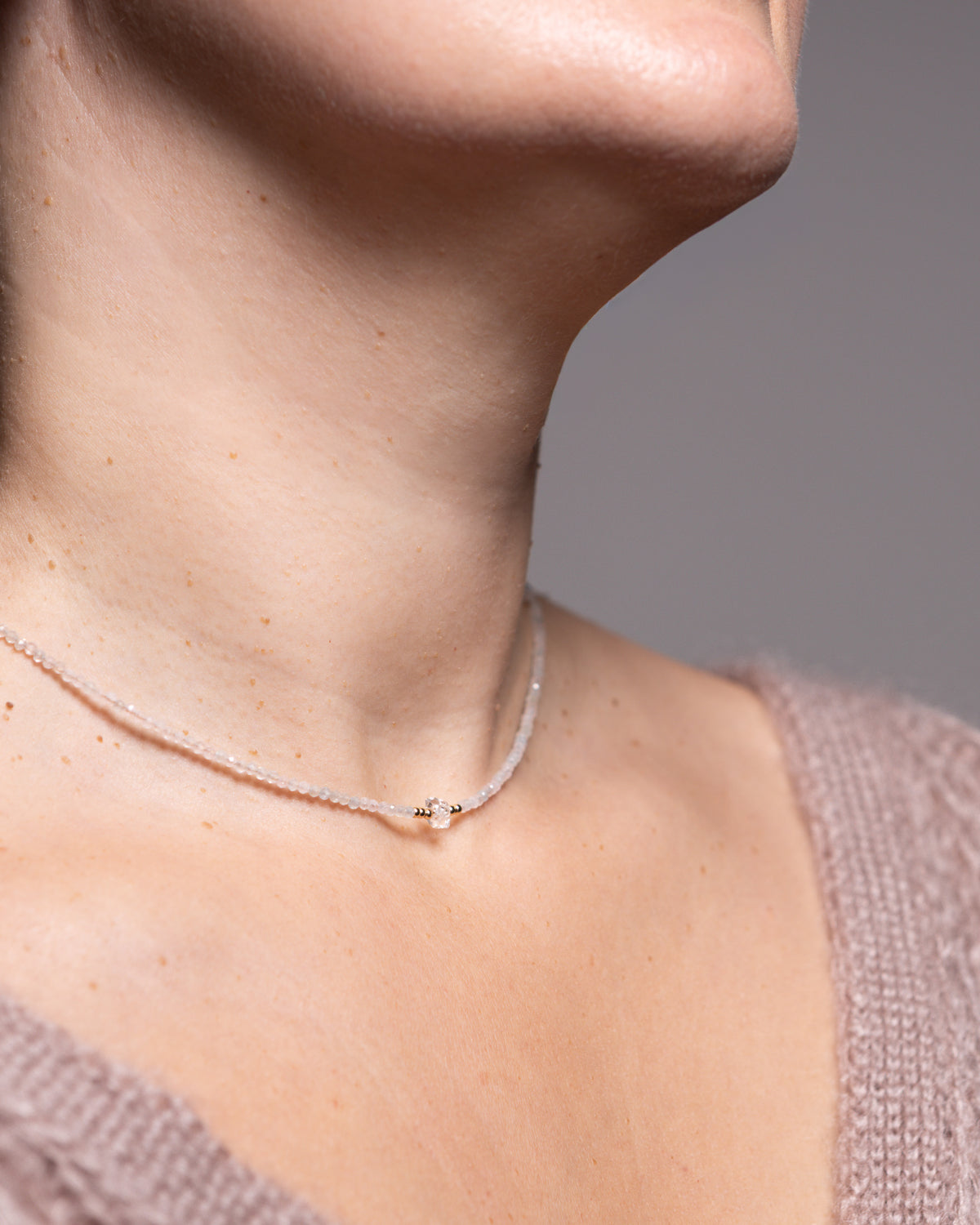 A close-up of a model's neck and upper chest wearing a delicate, thin silver chain necklace with a small central charm.