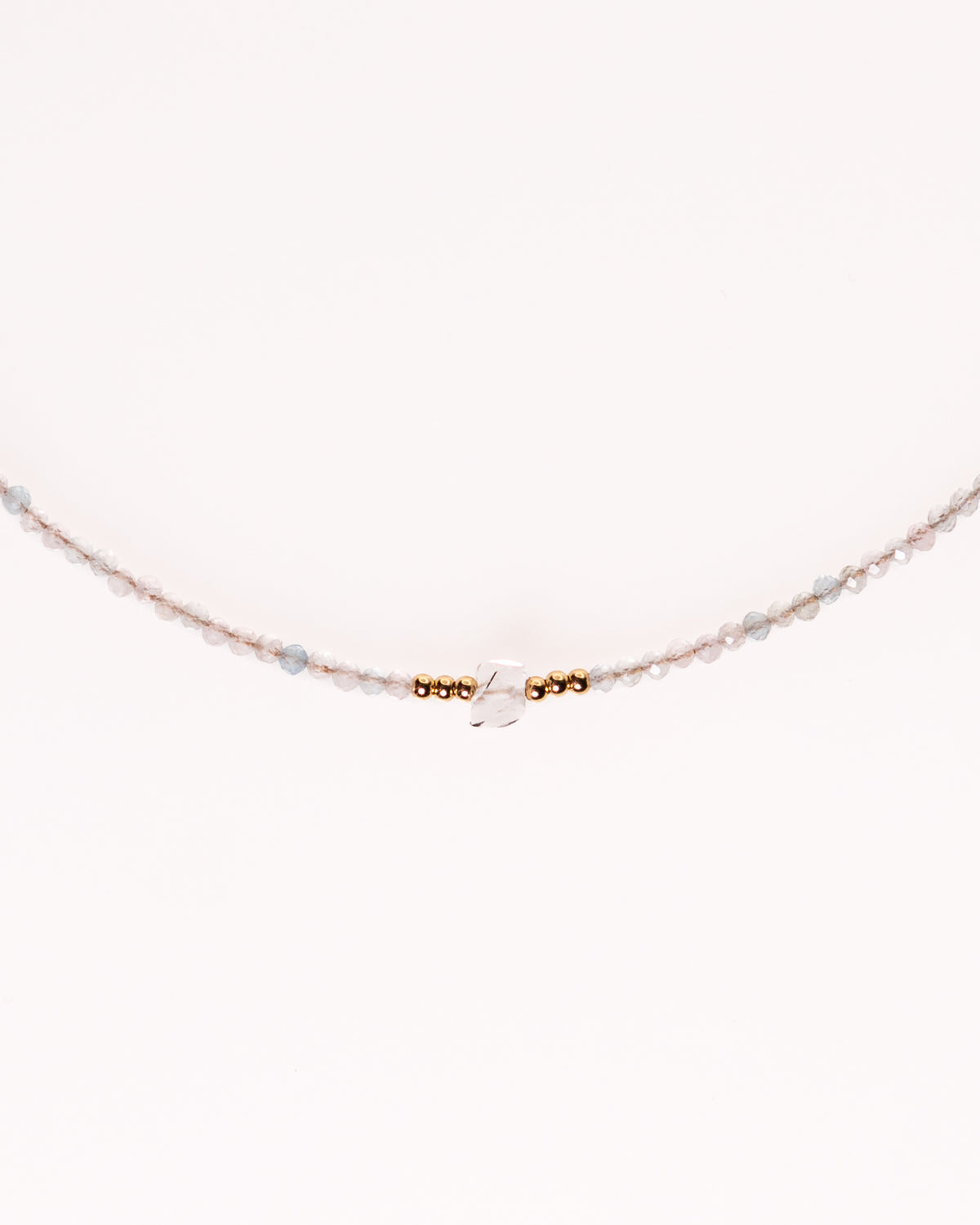 A delicate beaded necklace featuring small light pink and pale blue beads, accented by a central cluster of gold spacer beads and a clear faceted bead, shown against a plain white background.