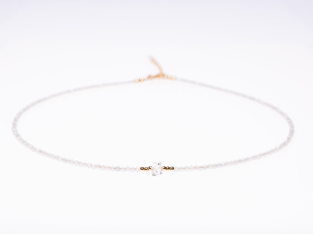 A delicate white beaded necklace with a central gold-toned bead cluster and a small clear crystal charm, displayed on a clean white background.